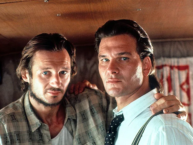 Two men stand side by side in a room, one in casual wear and the other in a white shirt and tie.
