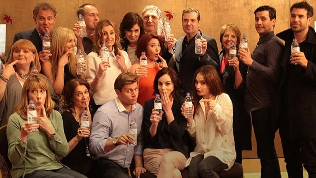 Group of Downton Abbey cast humorously posing with water bottles against a plain backdrop.