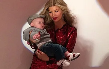 Woman in a red dress holding a baby wearing a gray cap and jeans.