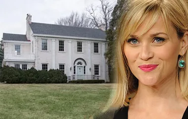 Reese Witherspoon smiling in front of her new white two-story Nashville home with a lawn.