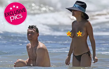 Couple enjoying the ocean, woman in a sunhat and bikini, man in swim shorts, exclusive photo watermark present.