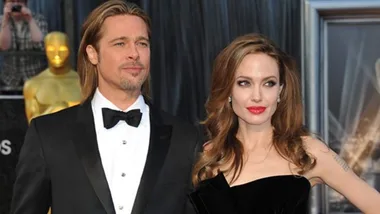 A couple elegantly dressed on the red carpet at a formal event, with a blurred background including a gold statue.