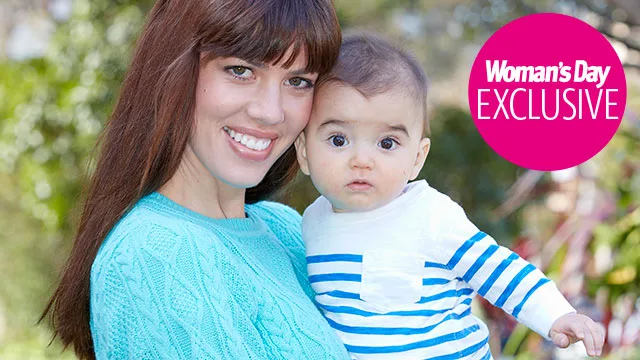 A woman in a blue sweater holds a baby in a striped shirt outdoors, with a "Woman's Day Exclusive" badge.