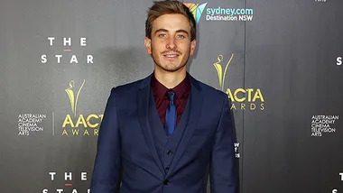 A person in a blue suit and tie poses at the AACTA Awards event backdrop.