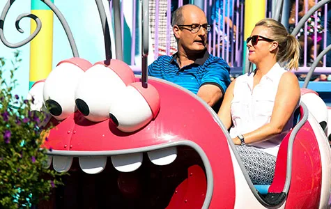 Adults enjoying a colorful ride at Universal Studios, seated in a whimsical car with large cartoon eyes.