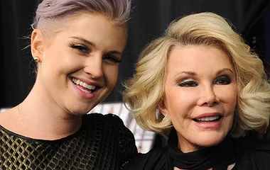 Women smiling together, one with blonde hair, the other with light purple hair, at an event.
