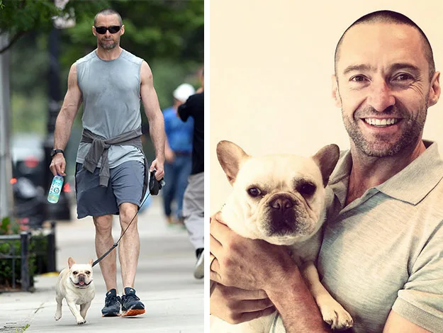 Man wearing sunglasses walking a small dog and holding the same dog, smiling indoors.