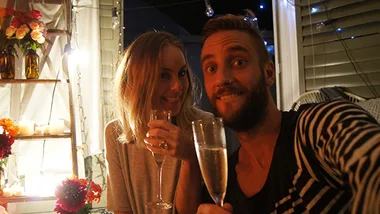 Couple celebrating engagement with champagne, surrounded by flowers and candles.
