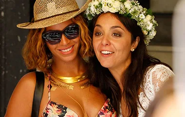 Beyoncé smiles with a bride in a floral dress and hat at a wedding, both appear joyful and relaxed.