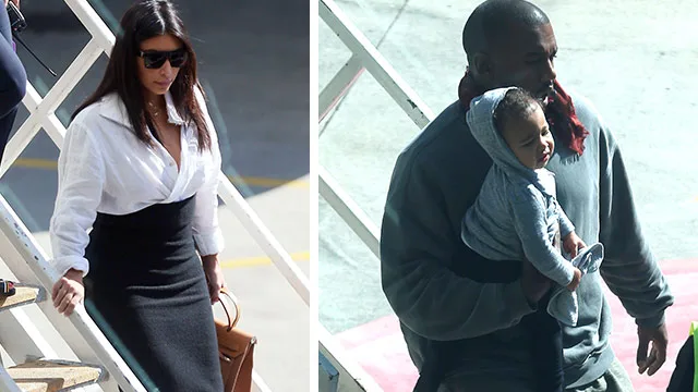 Man holding a baby in a hoodie and woman descending stairs in sunglasses, outside in a sunny setting.