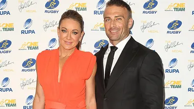 A couple in formal attire at a rugby event backdrop.