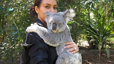 Kim Kardashian holding a koala in a lush outdoor setting.