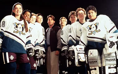 Reunion of "The Mighty Ducks" cast in hockey gear, forming a "Flying V" with coach, reminiscent of iconic movie scene.