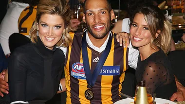 Delta Goodrem poses with an AFL player wearing a team jersey and medal at an event, smiling together.