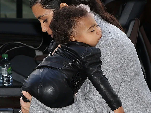 A person carrying a small child wearing a black leather outfit, inside a vehicle.