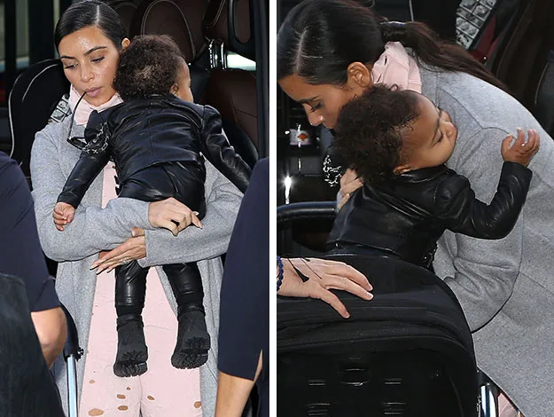 A woman in a gray coat holding a toddler in a black leather jacket against her shoulder.