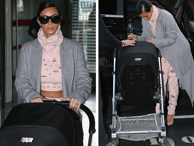 Woman in a pink distressed outfit and gray coat pushing a stroller, wearing sunglasses.