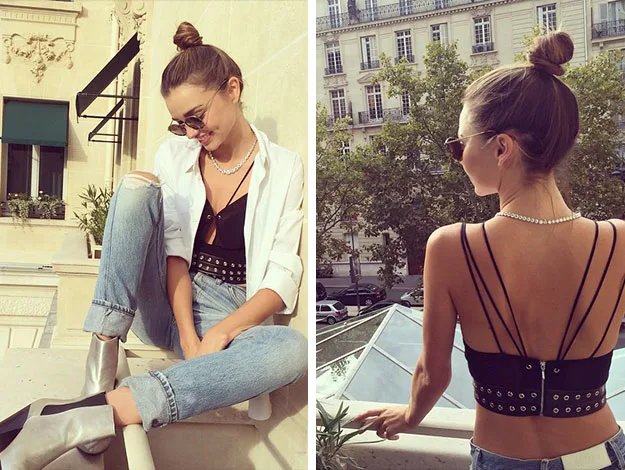Young woman on balcony in stylish outfit, wearing sunglasses and hair in a bun, looking relaxed and fashionable.