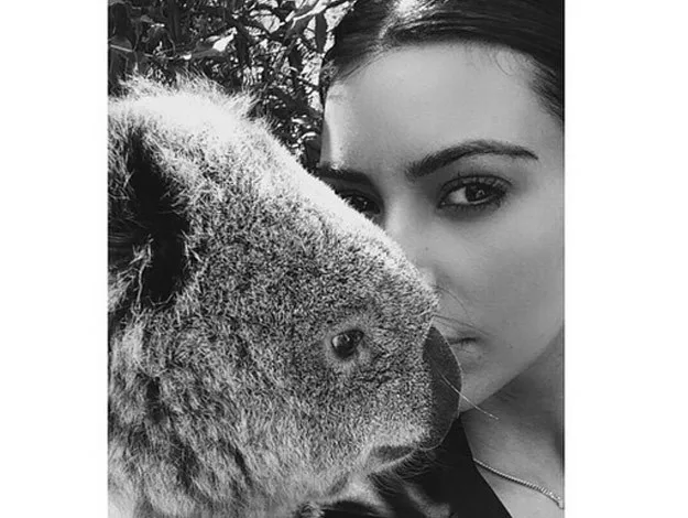 A woman poses closely with a koala in a black and white photo.