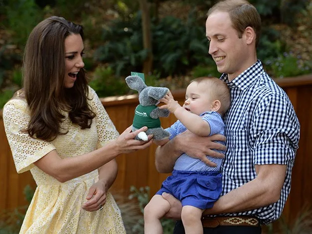 Three people smiling, one holding a baby with a toy, outdoors.