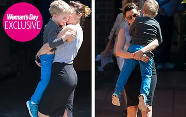 Mum carrying young boy in blue pants, wearing sunglasses, as they walk outside. Woman's Day EXCLUSIVE logo on image.