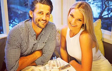A smiling couple poses at a dinner table by a window, creating a warm and intimate atmosphere.