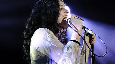Singer performing on stage, holding a microphone under dramatic lighting.