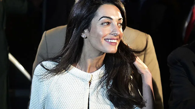 Amal Clooney smiling, wearing a white outfit, as she returns to work.