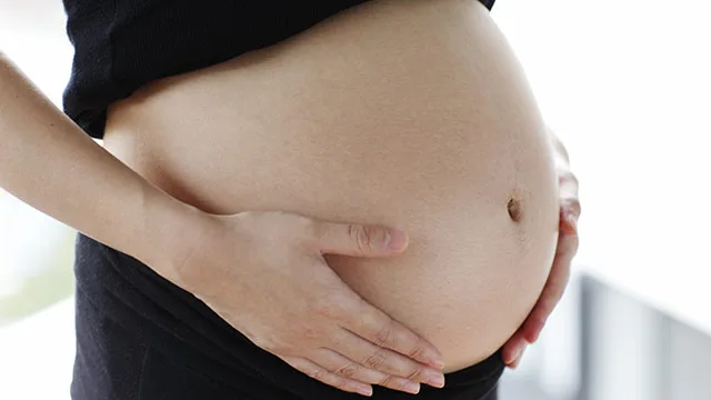 Pregnant woman holding her belly, wearing a black shirt, with a window background.