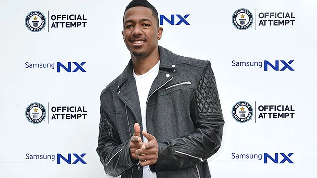 Nick Cannon posing at a Samsung NX and Guinness World Records event, smiling and gesturing with his hands.