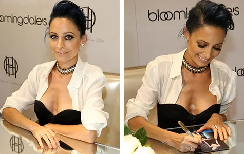 Nicole Richie at a jewelry launch event, sitting and signing autographs, wearing a black and white outfit with gold accessories.