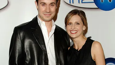 A smiling couple poses together at an event, wearing formal black attire against a branded backdrop.
