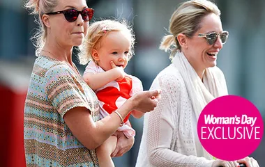 Women holding a toddler outdoors, all are smiling; Woman's Day Exclusive logo at bottom right.