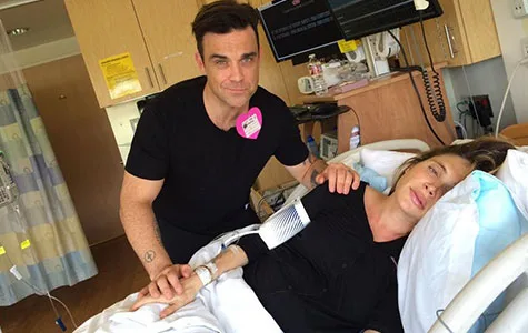 Couple in hospital room, man stands by bed comforting woman lying down, near medical equipment.