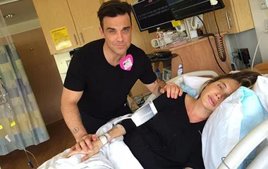Couple in hospital room, man stands by bed comforting woman lying down, near medical equipment.