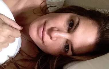 Cindy Crawford lying in bed, makeup-free, with a relaxed expression.