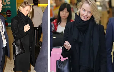 Businesswoman in oversized black outfit and scarf arrives at airport.