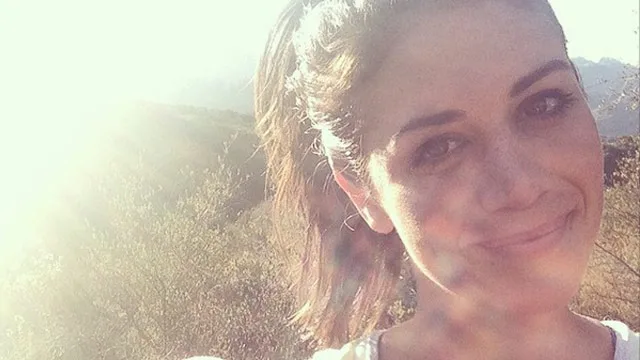 Smiling woman outdoors with sunlight in background.