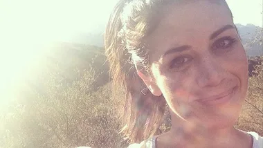 Smiling woman outdoors with sunlight in background.