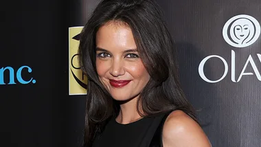 Actress in black dress smiling at a red carpet event.