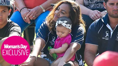 Woman holding a baby on her lap, surrounded by people, wearing matching navy shirts.