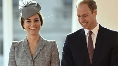 A smiling man and woman in formal attire, with the woman wearing a gray hat with decorative accents.