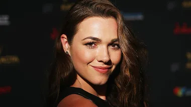 Actress Demi Harman smiling at a formal event with a dark background.