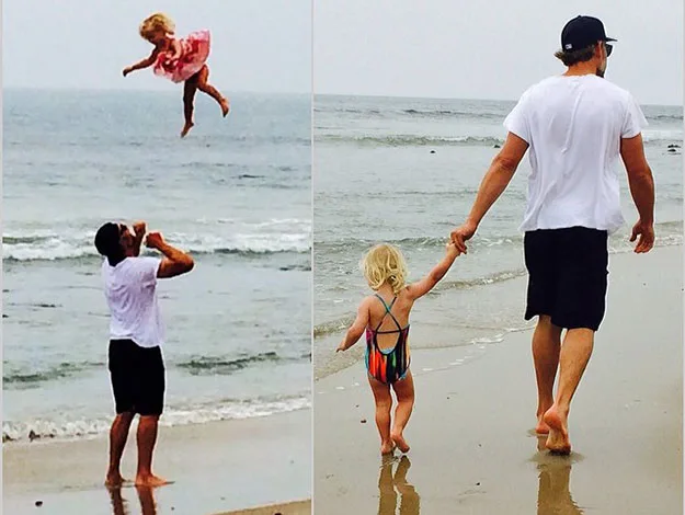 A man plays with a child on the beach; lifting her in the air, and walking hand in hand by the sea.