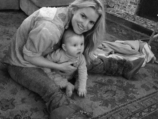 Woman sitting on the floor with a baby on her lap, both smiling, in a cozy living room setting.