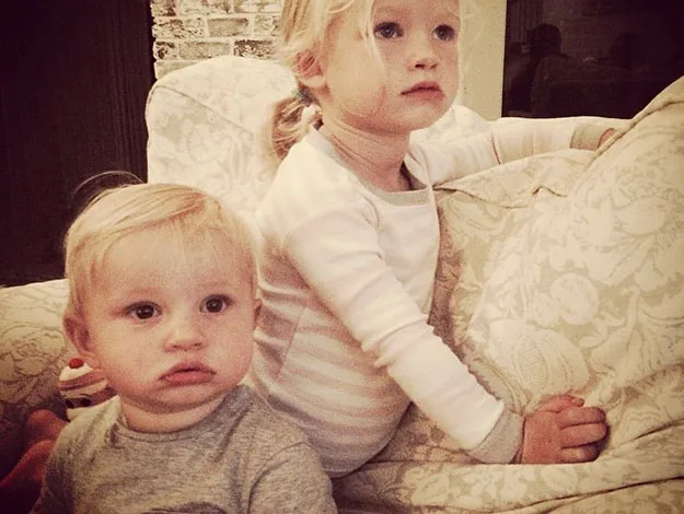 Two young children sitting on a patterned sofa, looking attentively towards something off-camera.