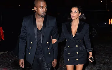 Couple in matching black outfits with gold buttons, walking arm in arm at night.