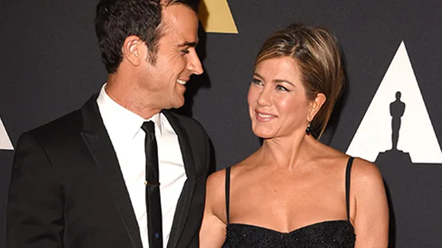 Two people in formal attire smiling at each other on a red carpet event.