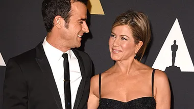 Two people in formal attire smiling at each other on a red carpet event.