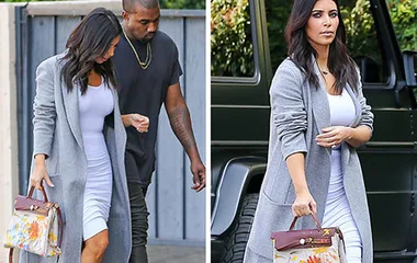 Kim Kardashian carrying a Hermès bag hand-painted by North West, wearing a gray coat and white dress, walking with a companion.
